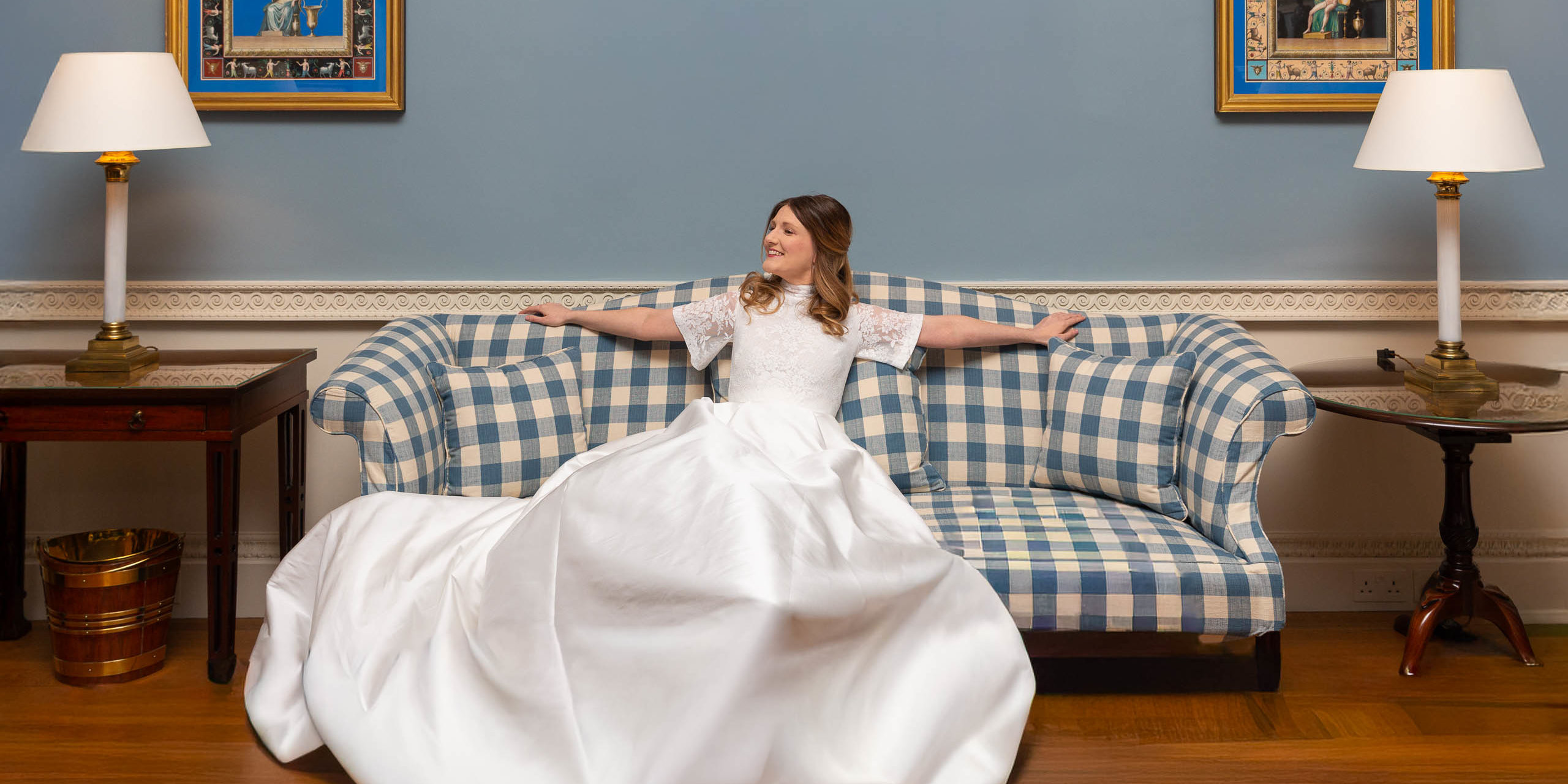 Bride sitting on a blue sofa in an elegant room before her wedding ceremony.