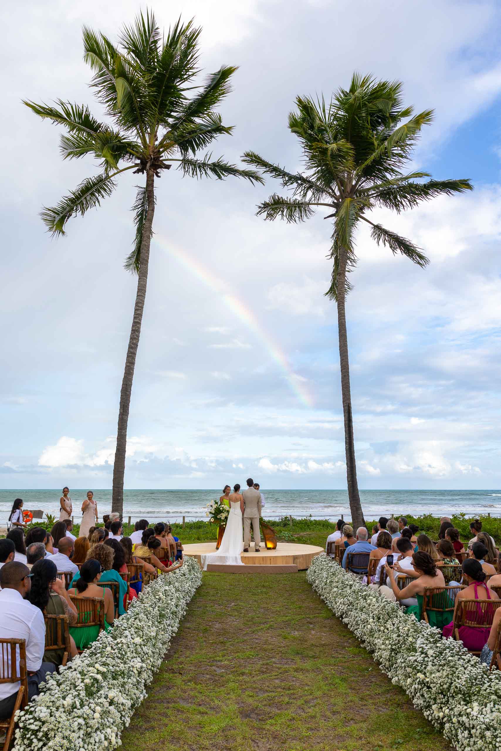 Destination beach wedding ceremony beneath a rainbow overlooking the ocean.