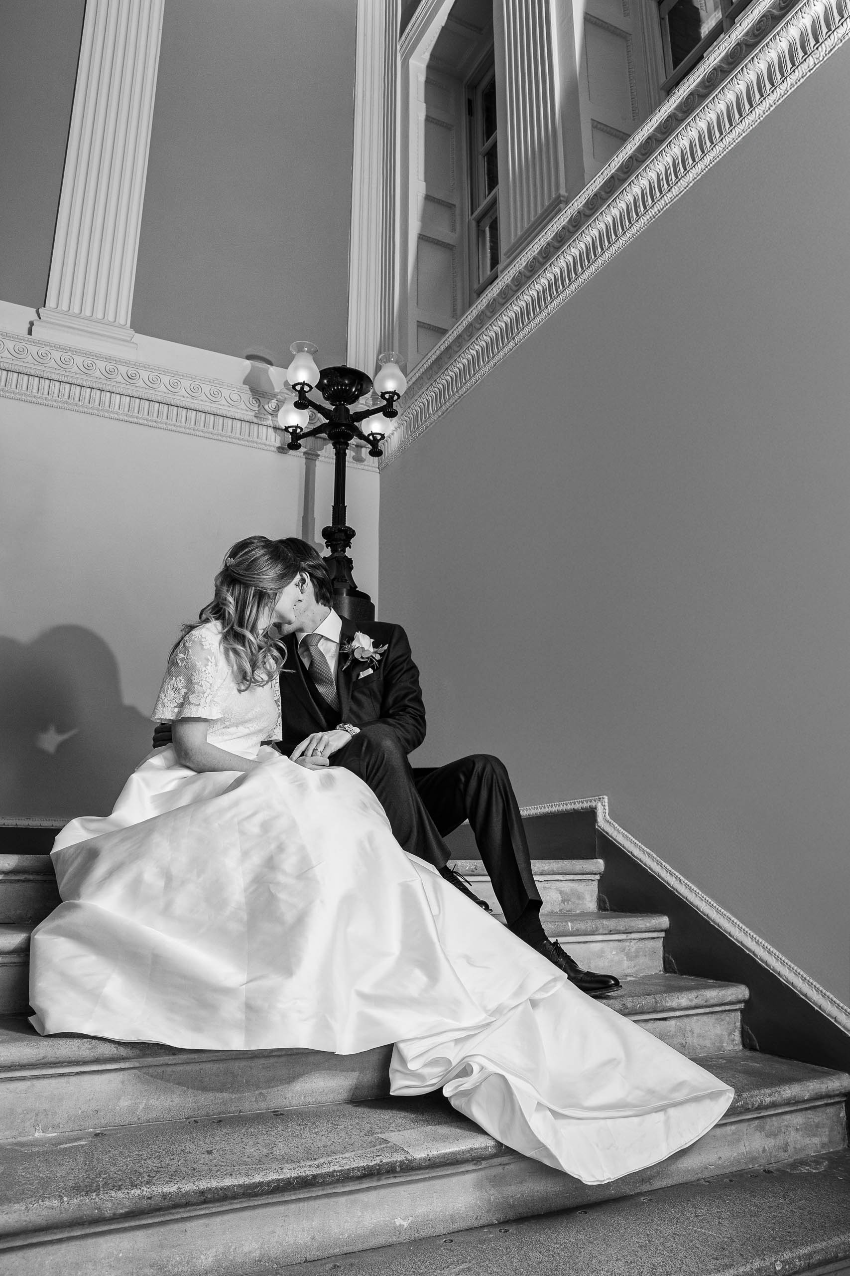 Bride and groom sitting together on the grand staircase inside Spencer House, sharing a quiet moment during their wedding day.