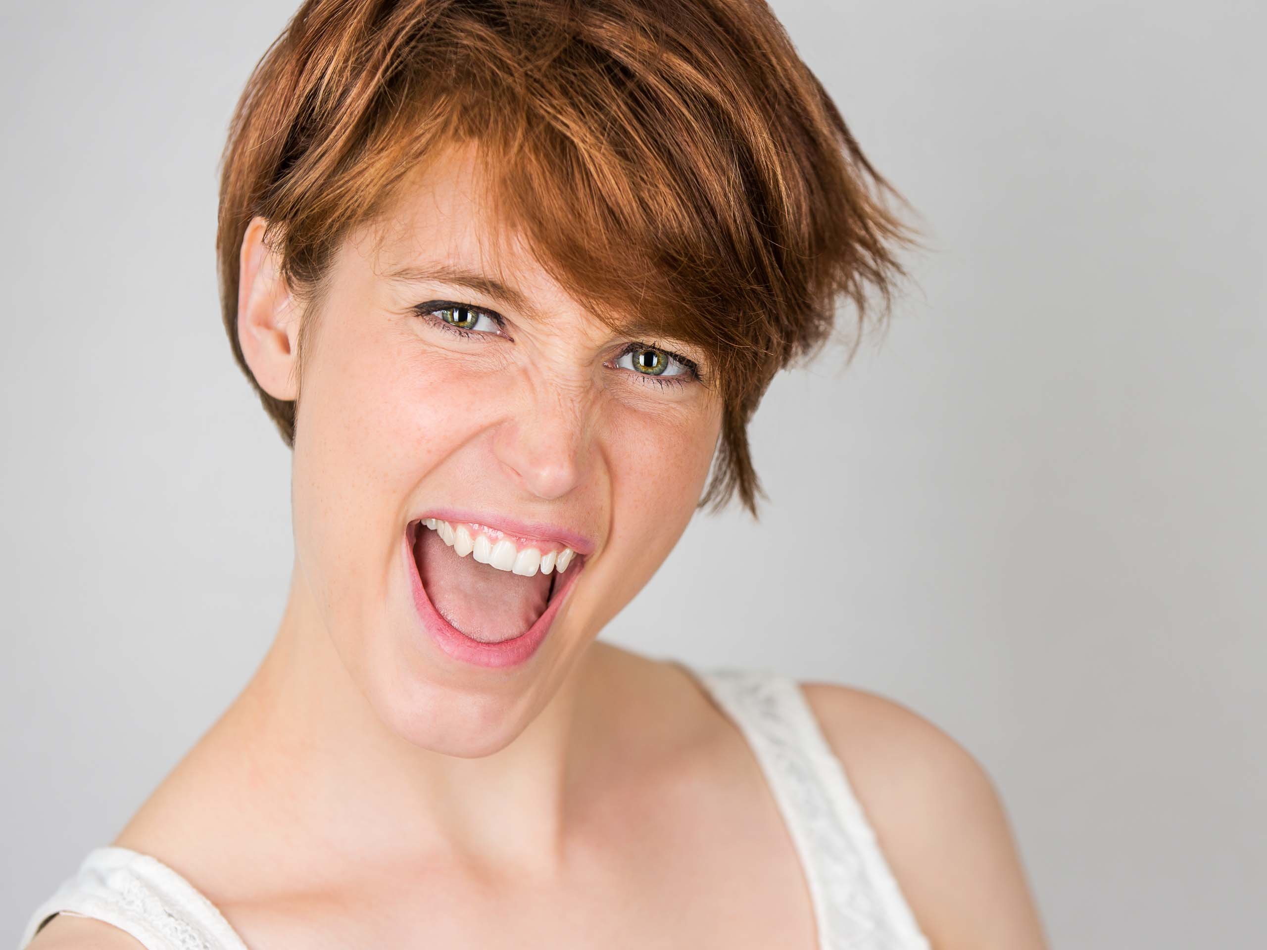 Expressive portrait of a woman smiling with a playful expression against a neutral background.