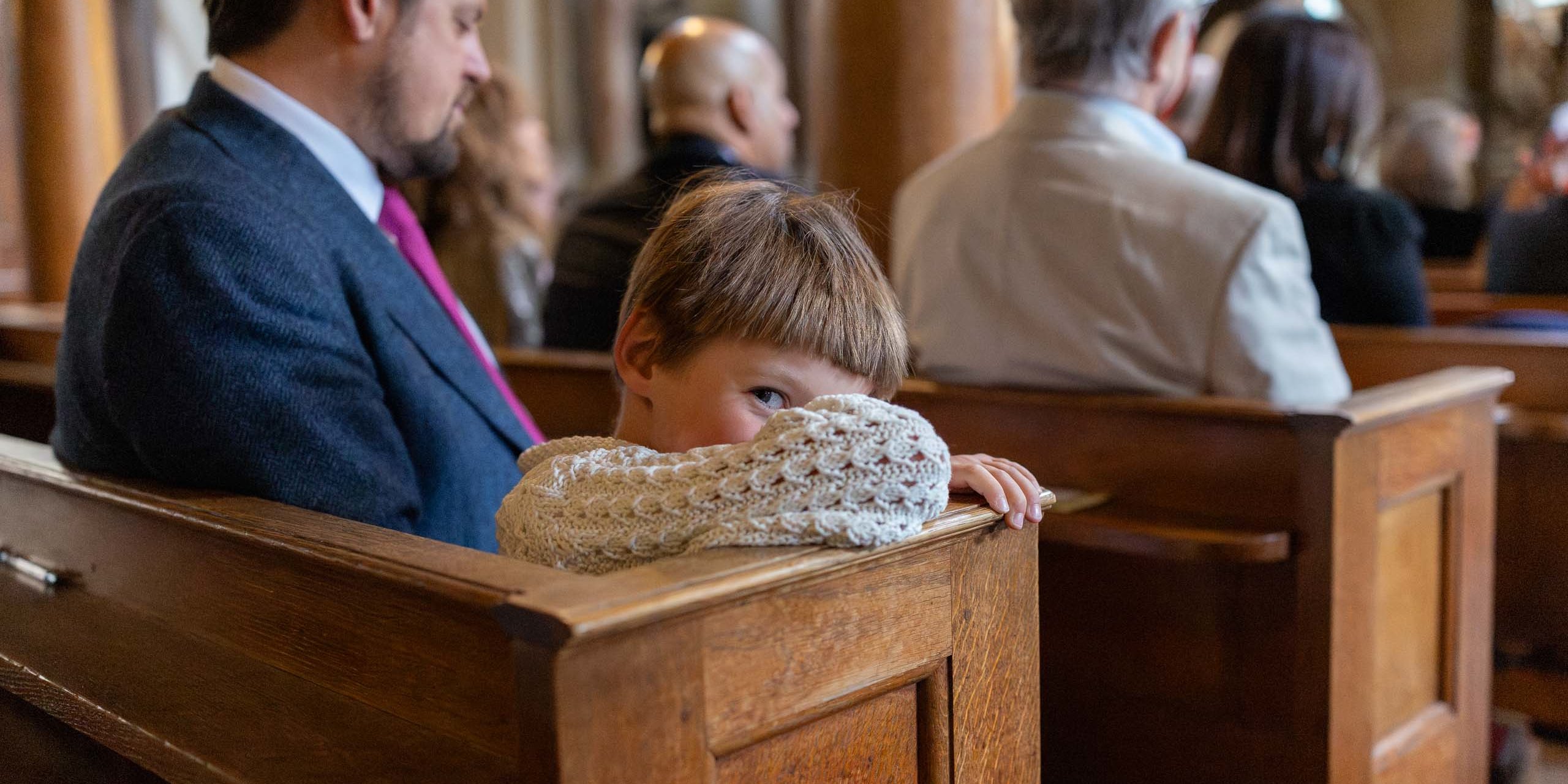 Guest peeking over a church pew during a wedding ceremony.