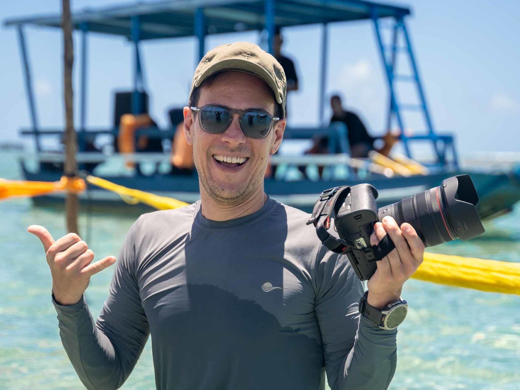 Matt Hodgkin holding a camera while standing in the sea during a destination wedding in Brazil.