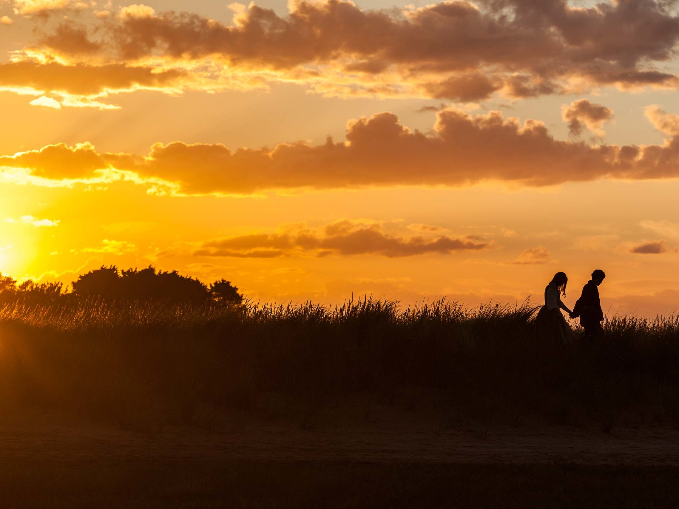 Silhouetted figures walking through tall grass at sunset during a film production.